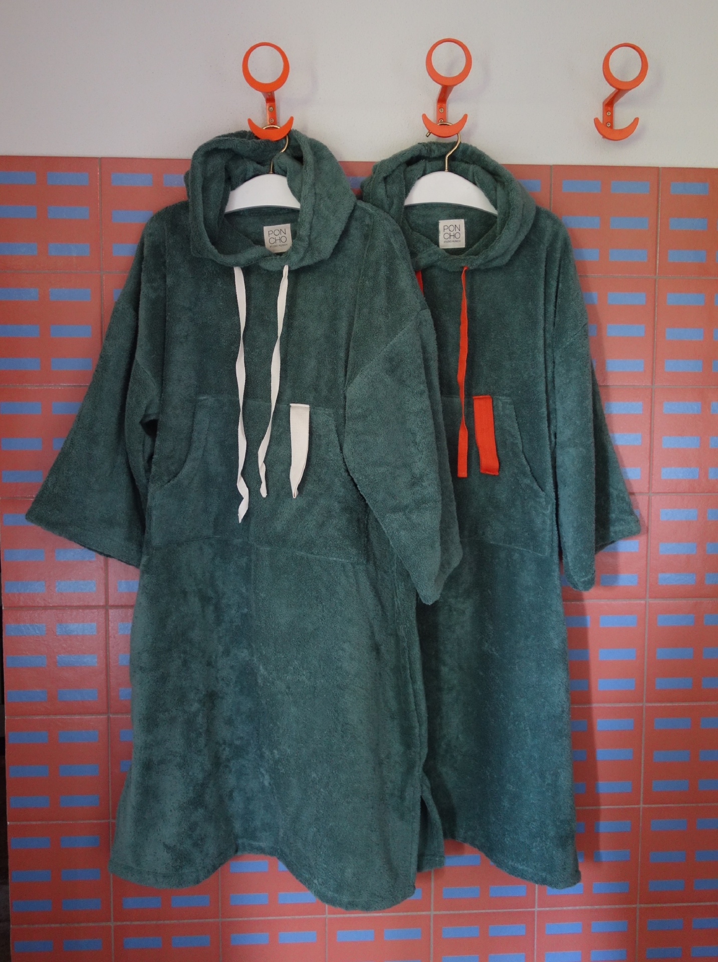 Two teal hooded ponchos hanging on a wooden wall